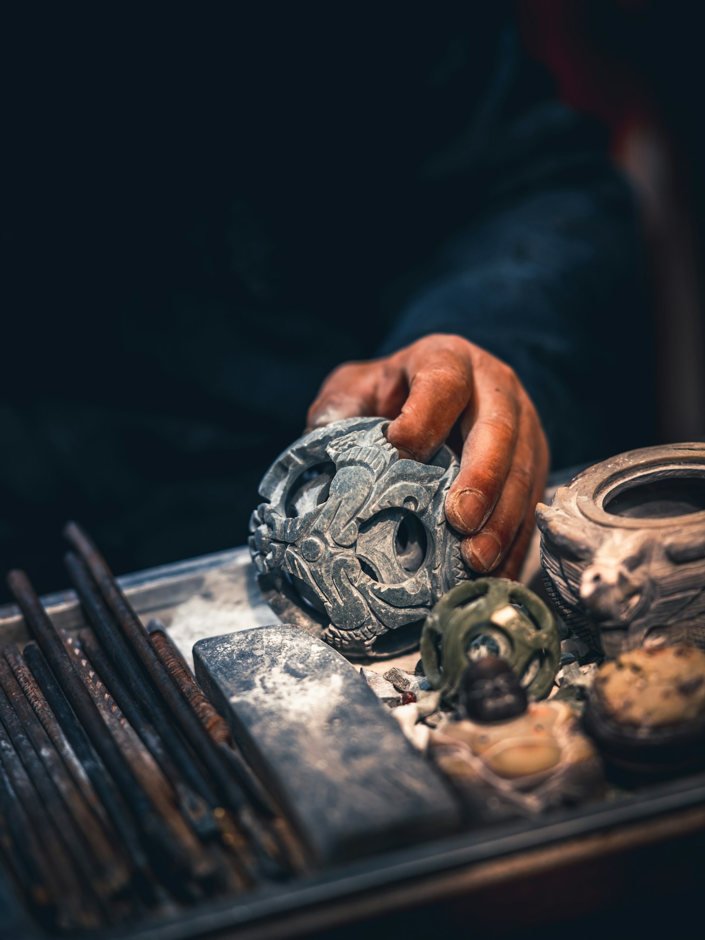 An artisan's hand carving an intricate stone sphere at Mount Qingcheng