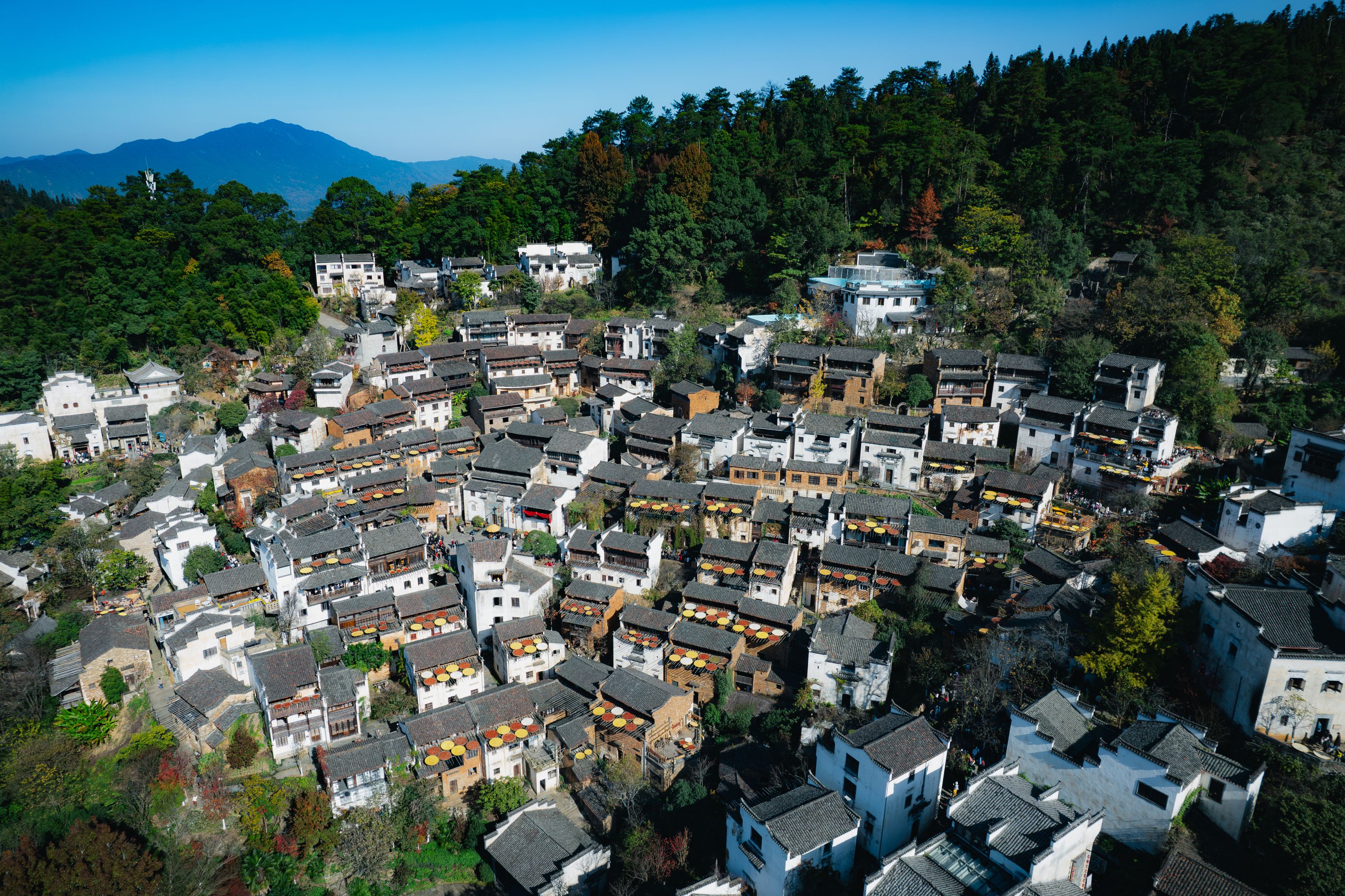 Sunlit traditional village in Wuyuan, with white walls, tiled rooftops and colourful drying baskets among green wooded hills beneath a blue sky